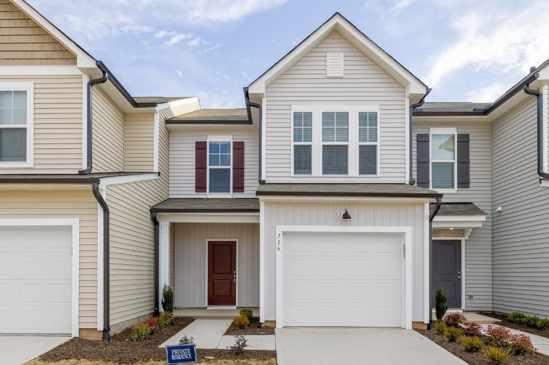 Modern townhouse with white siding, burgundy door, and two-car garage in residential community