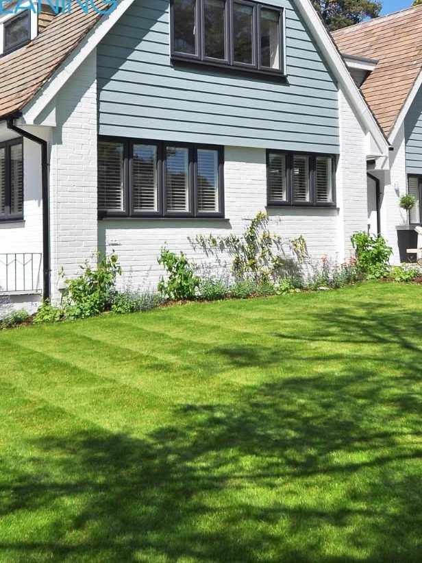 White cottage with black windows, manicured lawn, and garden plantings