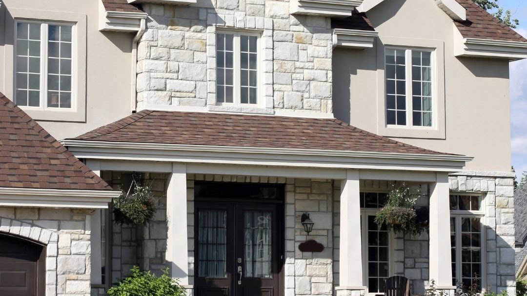Two-story stone and cream-colored residential home with dark roof and front porch