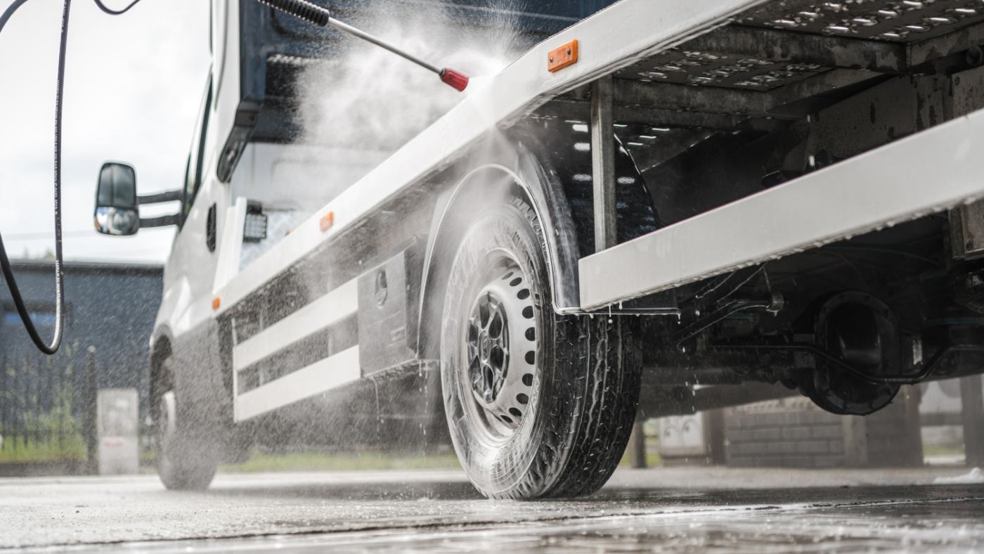White commercial truck being pressure washed at an outdoor facility
