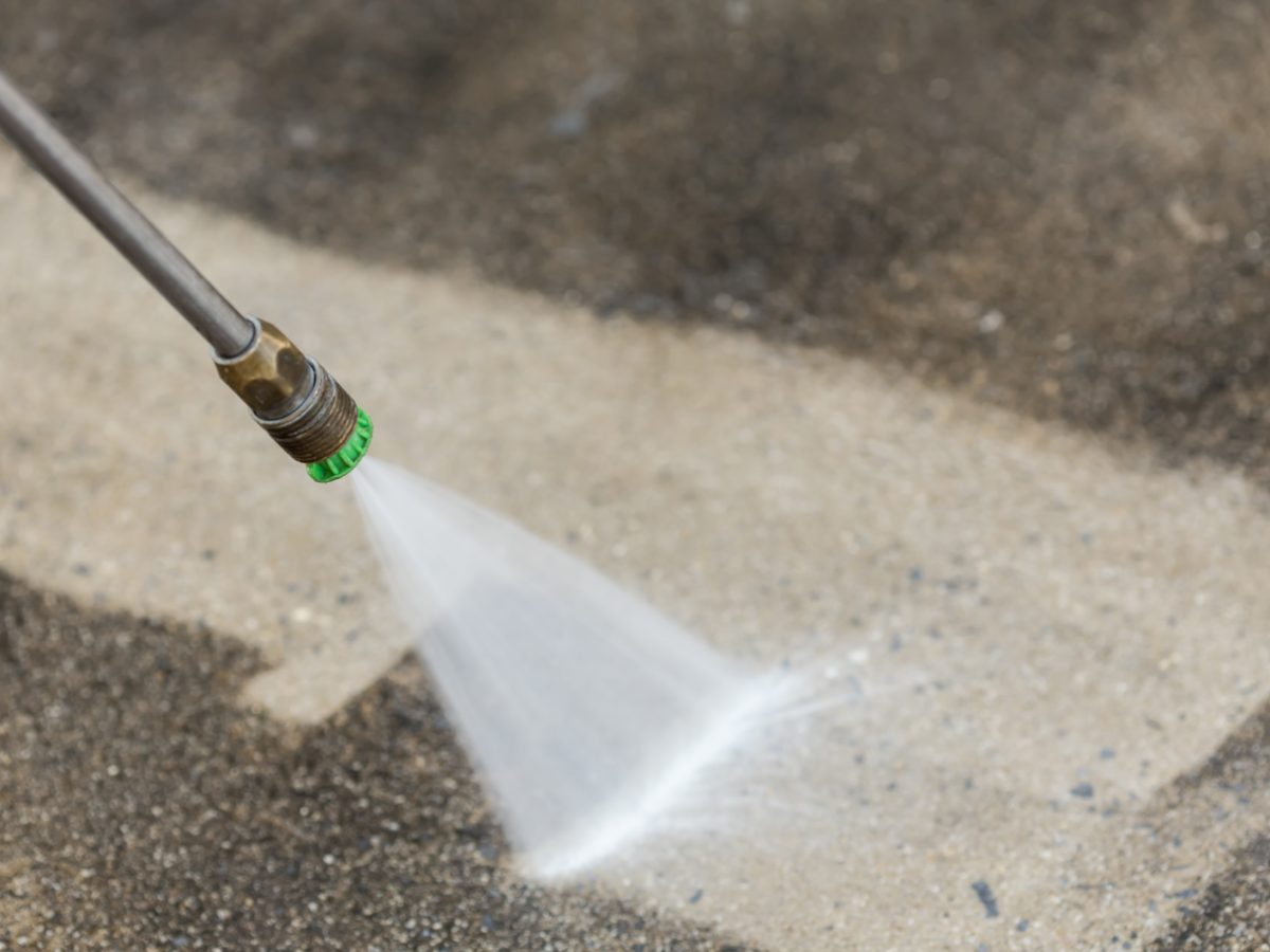 Pressure washer nozzle spraying water stream on concrete surface